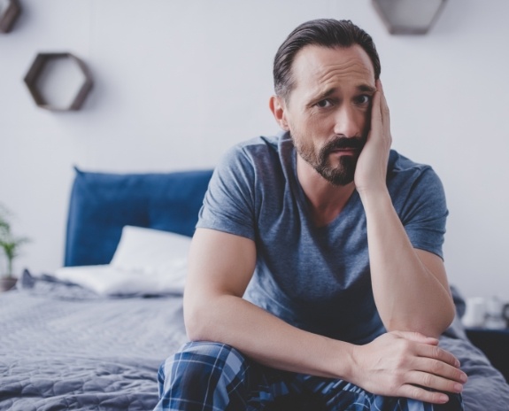 Man in need of emergency dentistry holding cheek in pain