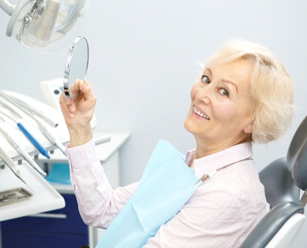Older woman with dental implants smiling into hand mirror