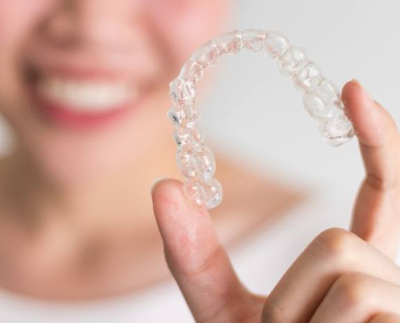 Hand holding an Invisalign clear braces tray