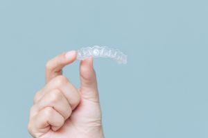 Person holding an Invisalign aligner against a light blue background.